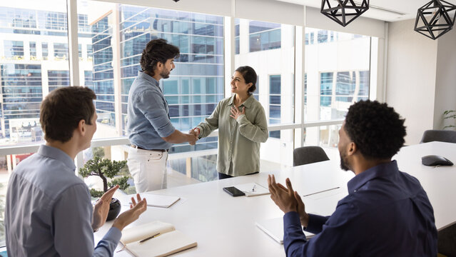 Boss praising proud Indian female employee, congratulating with corporate success, handshaking, express appreciation and recognition, colleagues clap hands, supporting mate during meeting in boardroom
