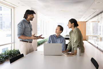 Teammates listen Indian middle-aged boss presenting new information, joint project updates, lead work-related discussion, collaborating on joint task, brainstorming, engaged in teamwork in coworking