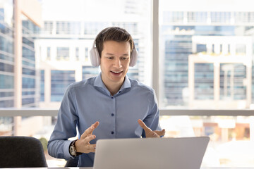 Fototapeta premium Young European businessman wear headphones engaged in videocall virtual meeting in office by business, take part in negotiations or online discussion with partners or colleagues. Digital communication