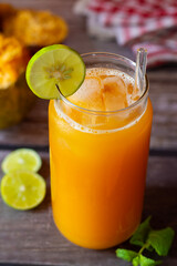 A refreshing glass of bael fruit juice garnished with lime and mint, accompanied by halved bael...