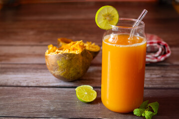 A refreshing glass of bael fruit juice garnished with lime and mint, accompanied by halved bael...