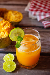 A refreshing glass of bael fruit juice garnished with lime and mint, accompanied by halved bael fruit and lime slices on a rustic wooden table.