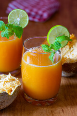 Two glasses of bael juice on a wooden table, garnished with lime and mint, surrounded by fresh...