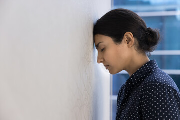 Close up Indian woman employee lean her head against wall in workplace, feel tired, dealing with...