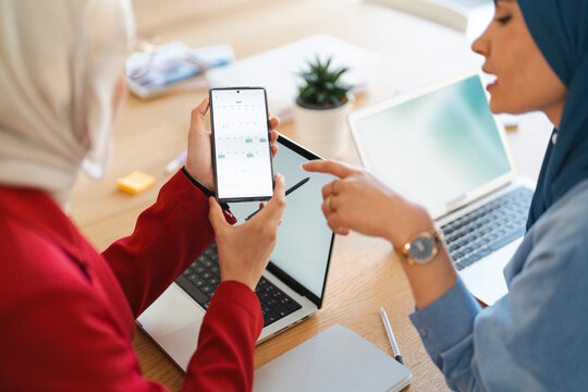 Two women are collaborating on a project, using a phone calendar and laptop to schedule meetings. They are working together to plan for the future.