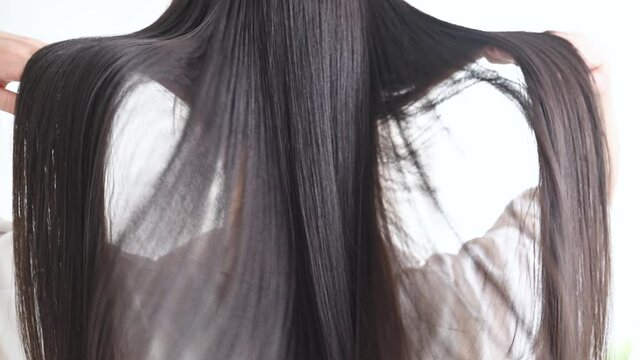 Long shiny black hair without face behind woman's back beautiful straight hair with cuticles slow animation of hair lifting