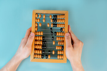 The man's hands holds wooden old abacus on the blue table background. The concept of accounting and...