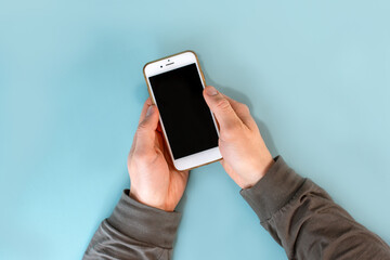 The man's hands are holding a smartphone with a black screen on a blue table background. Close up, point of view shot.