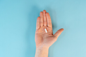 A man's hands hold a pill capsule on a blue table background. The concept of diseases and treatment. Close up, point of view shot.
