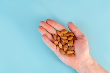 A man's hand holds a handful of almonds on a blue table background. The concept of healthy...
