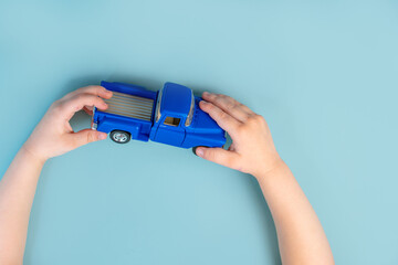 Children's hands of a little boy or girl hold a blue toy car on a blue table background. Close up, point of view shot.