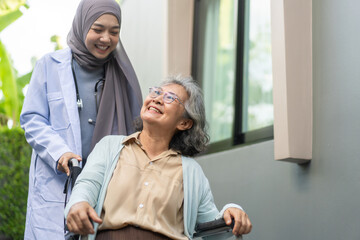 Muslim female doctor caregiver assisting elderly patient in wheelchair, healthcare service, senior care concept, medical support, rehabilitation, health professional with stethoscope providing help
