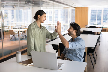 Two happy Indian employees giving high five during meeting in coworking office, greeting each...