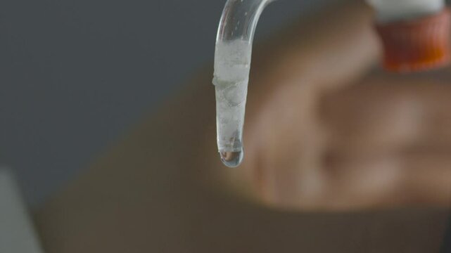 Detailed close-up of a drop of liquid descending from a burette in a laboratory setting.