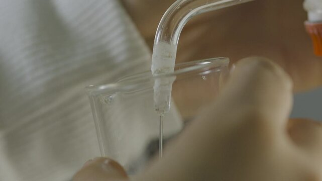 Close-up of a clear liquid gently being drawn from a burette into a test tube in a laboratory setting.