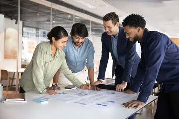 Group of smiling multiethnic people reviewing documents, analyzing infographic data, engaged in...