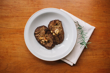 empal gepuk, indonesian style sweet and spicy fried beef dish on white plate, napkin and wooden background