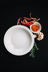 empty white plate with spices and herbs on black background