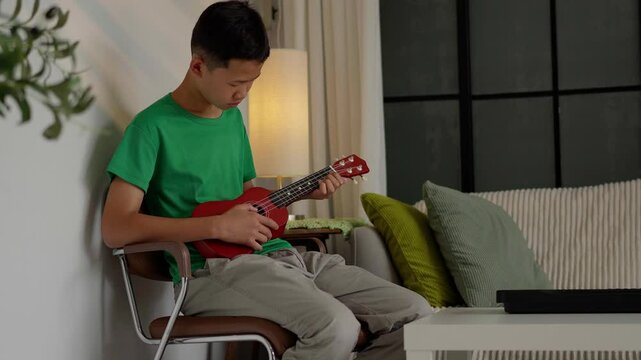 Asian boy learning to play ukulele
