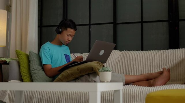 Asian boy studies online on laptop at home