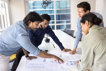 Group of diverse professionals engaged in active discussion gathered around conference table with various charts and document, working together to analyze data and make decisions. Analytics, planning