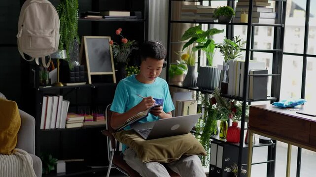 Asian boy studies online on laptop at home