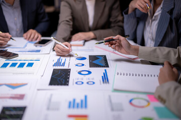 A group of people are sitting at a table with a lot of papers and graphs