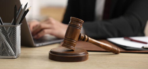 Closeup of judge working on laptop at table in office, focus on gavel. Banner design