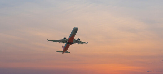 Airplane flying above dramatic sunset sky background.