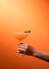 Hand holding orange cocktail against orange backdrop