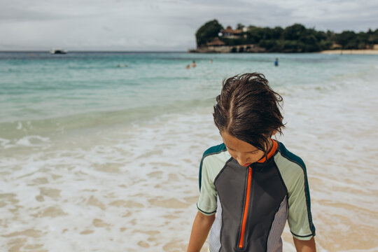 Boy enjoying a day at the beach while looking down at the ocean waves