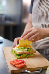 Chef adding cheese slice to a fresh sandwich in a commercial kitchen.