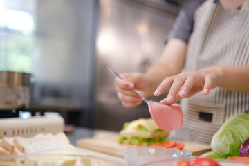 Obraz premium Close-up of chef adding sliced ham to a sandwich
