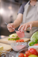Close-up of chef adding sliced ham to a sandwich