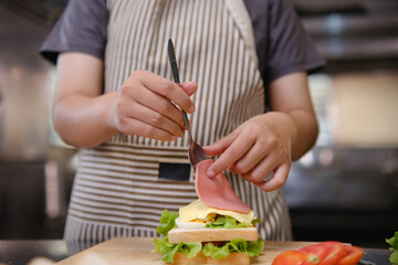 Close-up of chef adding sliced ham to a sandwich
