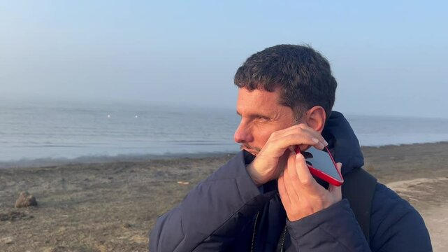 A blind man using his mobile phone on the empty beach