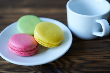 Colorful macaroons and cup of coffee on wooden table.