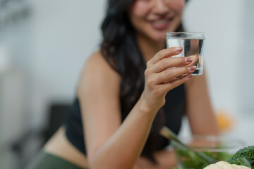 Happy young woman drinking a glass of fresh water and smiling while eating a healthy salad with vegetables, promoting a healthy lifestyle and hydration