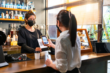 Small business entrepreneur coffee shop cafe restaurant. Happy Asian woman customer buy coffee with using smartphone scan QR code on cashier counter making online banking payment at coffee shop.