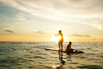 Side view sisters paddle boarding at sunset Gulf of Mexico