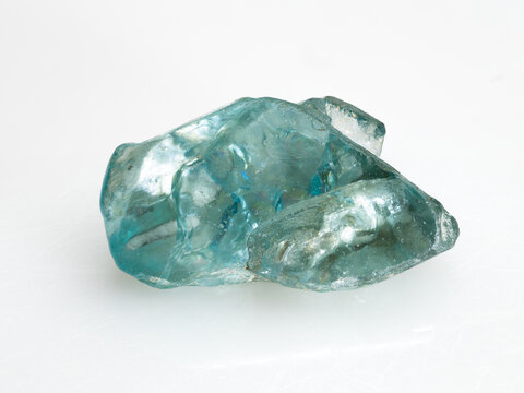 A close-up studio shot of a raw, translucent blue natural zircon crystal against a dark background showcasing its irregular facets and internal reflections
