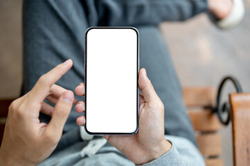 A hand holding smartphone with finger pointing at white screen, sitting cross legged on chair.