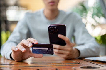 A man holding smartphone and other holding a credit card while sitting at wooden table in cafe.