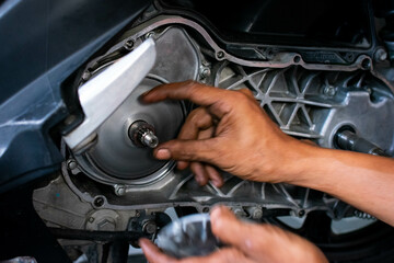 Close up of a mechanic's hands working on a scooter's CVT transmission system, focusing on the front pulley shaft during maintenance