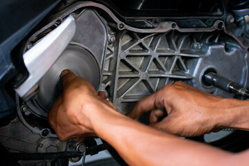Close up of a mechanic's hands working on a scooter's CVT transmission system, focusing on the front pulley shaft during maintenance