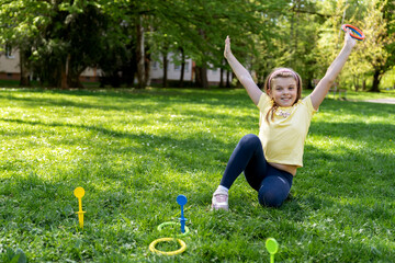Joyful child sitting on the grass with raised arms, enjoying a summer day, playing ring toss in the...