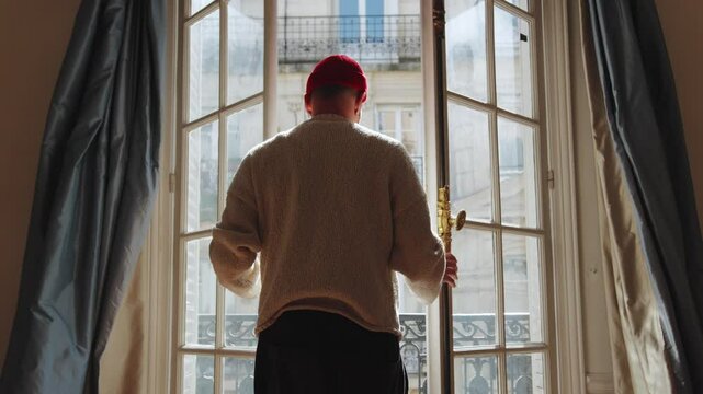 Man opening curtains and balcony doors in parisian apartment