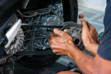 Close up of a mechanic’s hand adjusting the rear pulley axle of a scooter’s CVT transmission system during maintenance