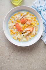 Plate of corn chowder with crab on a beige stone background, vertical shot with space, flat lay