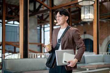 Brown suit man with glasses walking while holding a coffee cup with notebook and laptop the in cafe.